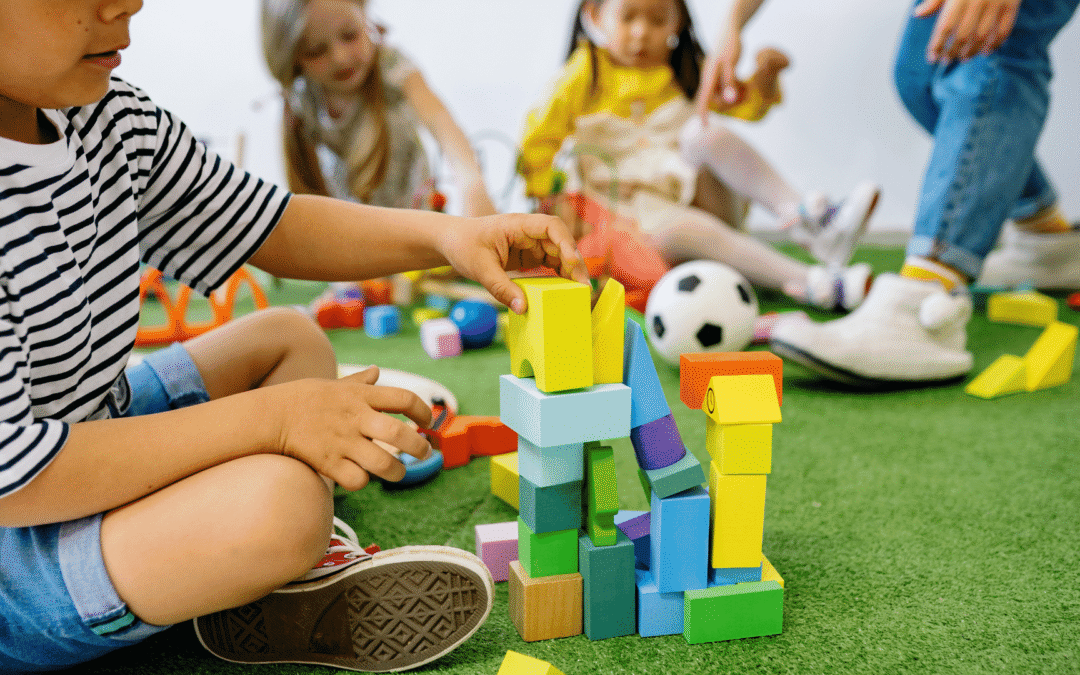 Unlock fun activities for kids as children sit on a green mat and build colorful block towers in a playroom